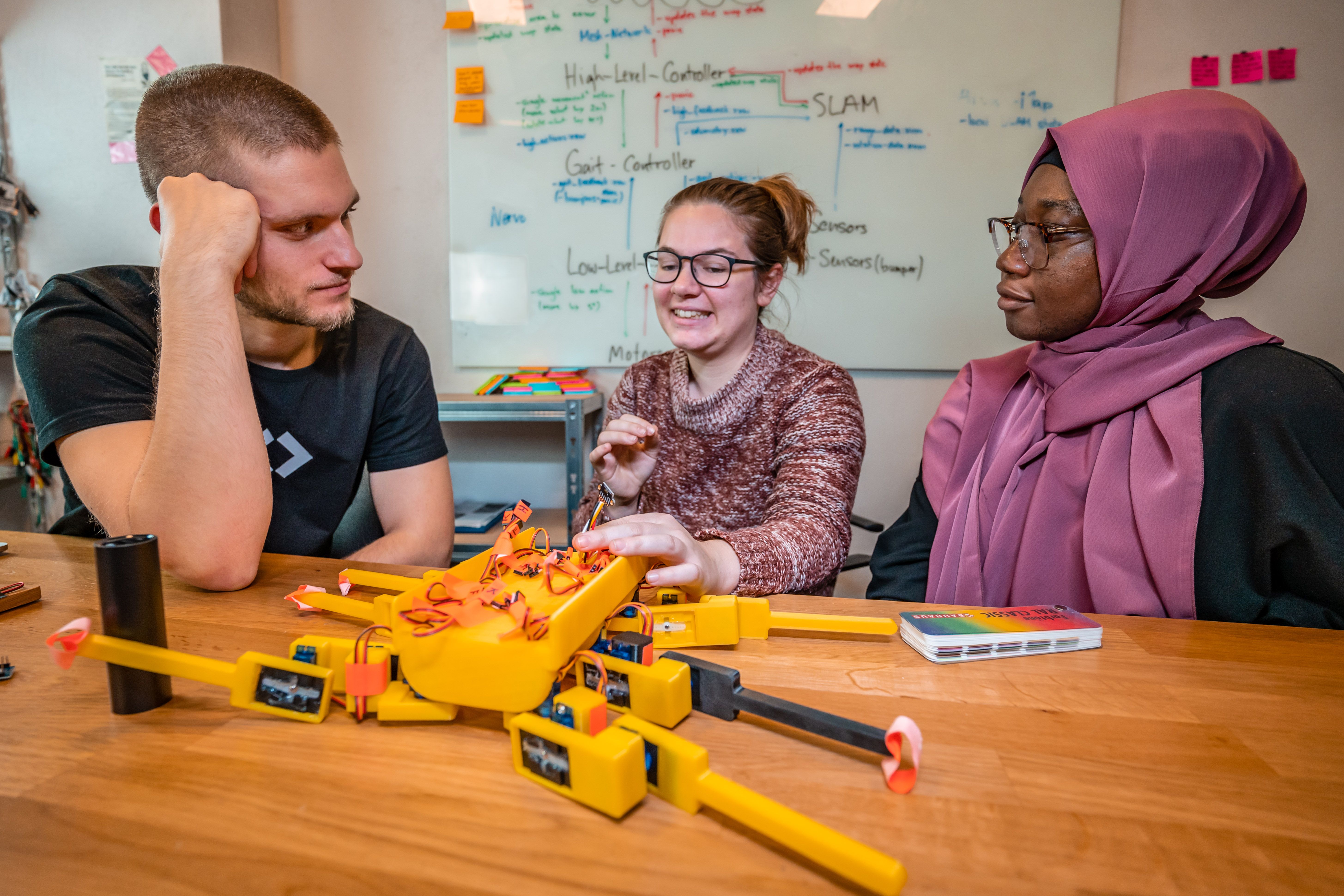 Three CODE students working together on a robotics prototype at a whiteboard