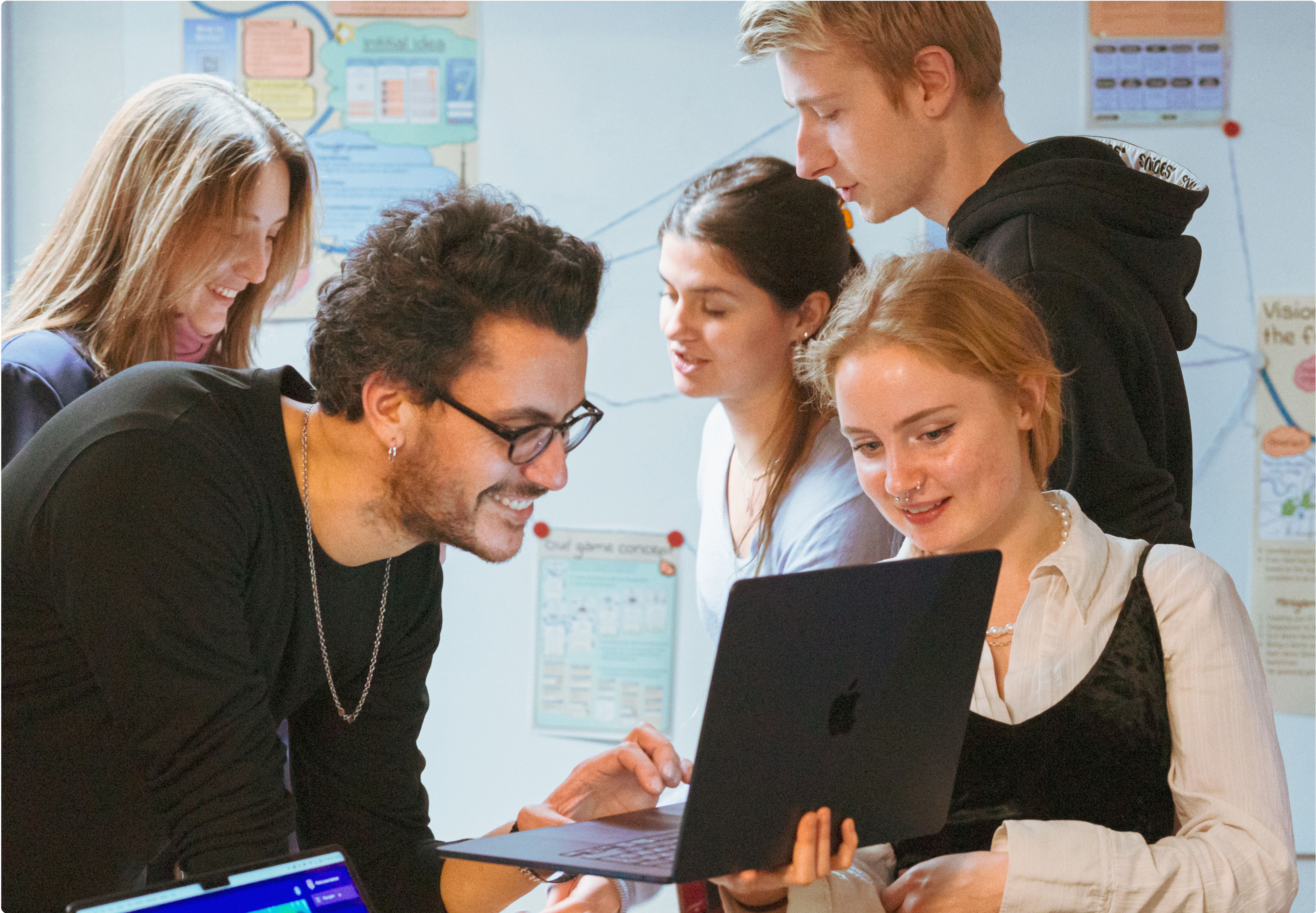 Five CODE students collaborating around a MacBook